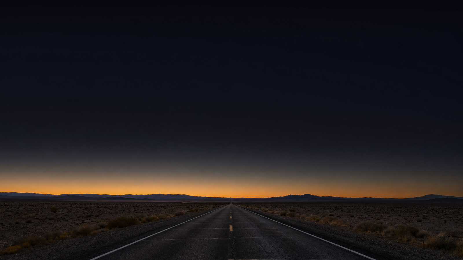 Straight two-lane desert highway at dusk under a dark, open sky